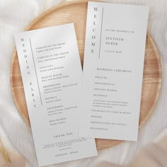 two white wedding programs sitting on top of a wooden plate