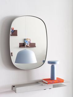 a mirror hanging on the wall next to a shelf with a lamp and book in front of it