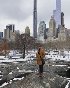 a man standing on top of a large rock in the middle of a snow covered park