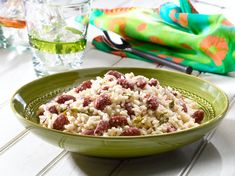 a green bowl filled with rice and meat on top of a table next to a glass of water