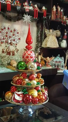 a christmas tree made out of ornaments on a table in front of a shelf filled with other holiday decorations