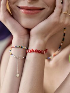 a woman with her hands on her face and bracelets around her neck, smiling at the camera