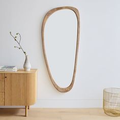 an oval wooden mirror hanging on the wall next to a sideboard with a vase