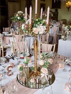 a table topped with lots of tables covered in pink and white flowers next to tall candles