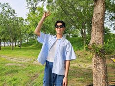 a man standing next to a tree with his hand up in the air while wearing sunglasses