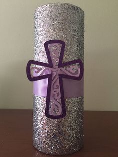 a purple and silver candle with a cross on the top is sitting on a table