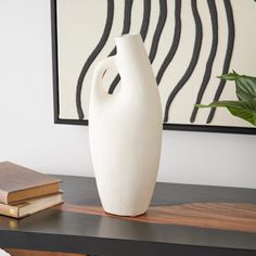 a white vase sitting on top of a wooden table next to a book and plant