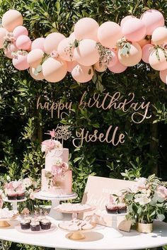 a birthday cake and cupcakes are on a table with pink balloons above it