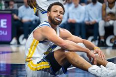 a basketball player is sitting on the court with his foot in the air while people watch