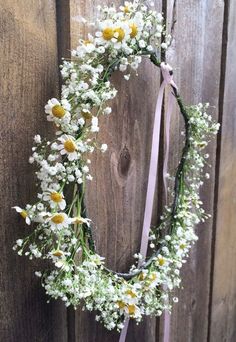 a wreath with daisies and baby's breath hanging on a wooden fence