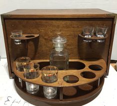 an old fashioned wooden case with glasses and shot glasses on the bottom, in front of it