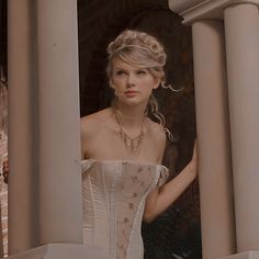 a woman in a white corset standing next to some pillars and looking at the camera