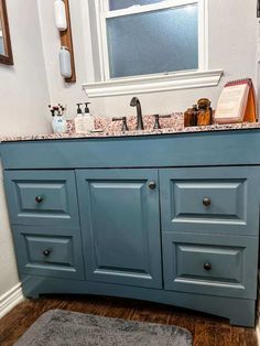 a bathroom vanity with blue cabinets and marble counter tops, along with a rug on the floor