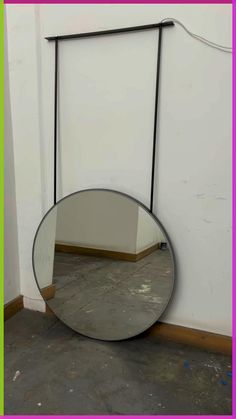 a round mirror sitting on top of a floor next to a wall