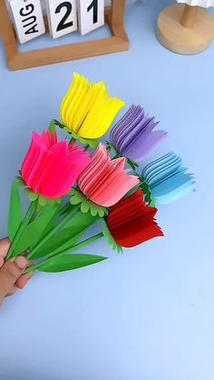 someone is holding up some paper flowers in front of a table with calendars on it