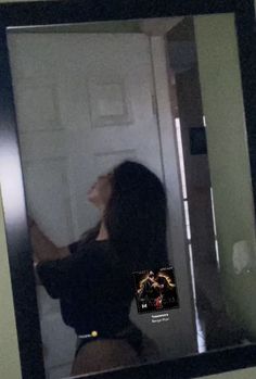 a woman standing in front of a mirror with her hand on the door knobs