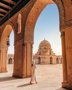 a woman standing under an archway in the middle of a courtyard with arches and domes