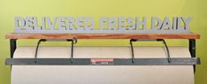 a metal sign that says deliver fresh daily on top of a wooden bench in front of a green wall