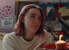 a woman holding a plate with a cupcake on it and a lit candle in her hand