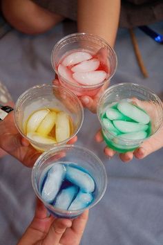 three people holding small cups filled with colored jello and marshmallows in their hands