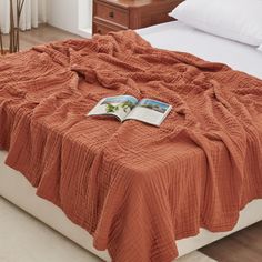 an open book is laying on the edge of a bed with orange blankets and pillows