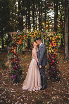 a bride and groom kissing in front of an arch with colorful flowers on it at their wedding