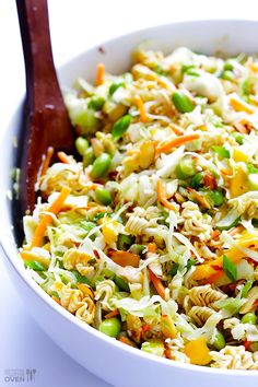 a white bowl filled with pasta and veggies next to a wooden serving spoon