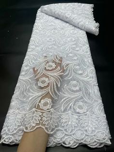 a white lace fabric with flowers on it and a hand reaching for the top one