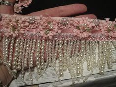 a hand holding a piece of pink fabric with pearls and flowers on it