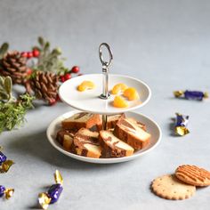 three tiered plate with orange slices and crackers on it, surrounded by christmas decorations