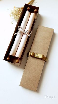 an open box with two rolled up candles in it next to some dried flowers on the table