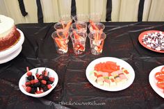 a table topped with plates and bowls filled with desserts next to cake on top of a black cloth covered table