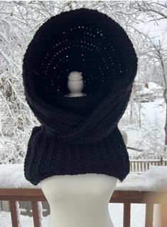 a white mannequin wearing a black knitted hat and scarf in the snow