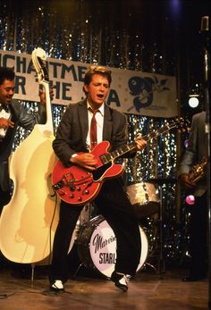 two men in suits are playing guitars on stage