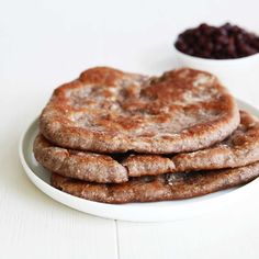 three pancakes on a white plate with raisins in the background