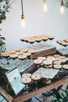 an assortment of desserts and wine glasses on a wooden table with hanging light bulbs