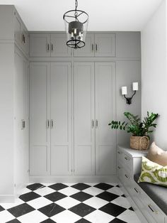 a black and white checkered floor in a room with gray cupboards, green plants, and a chandelier