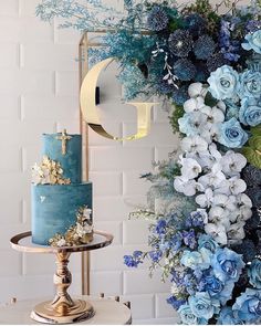 there is a blue cake with flowers on it and a gold stand next to the wall