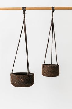 two hanging planters on a wooden bar against a white wall, one is brown and the other is black