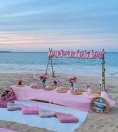 a birthday party setup on the beach with pink flowers and candles in front of it