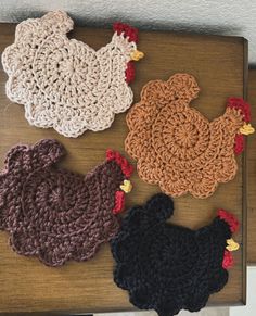 four crocheted chicken coasters sitting on top of a wooden table