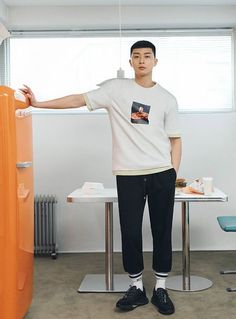 a man standing in front of a table with an orange refrigerator behind him and his hand on the door handle