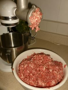 a white bowl filled with meat next to a mixer