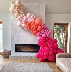 a living room filled with lots of pink and orange balloons hanging from the ceiling next to a fire place