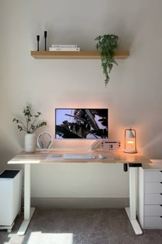 a desk with a computer on it and some plants in the corner next to it