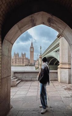 a man standing in an archway looking at the city skyline with big ben in the background