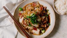 a white plate topped with food next to rice and chopsticks