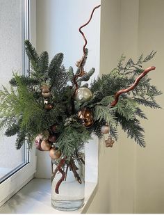 a vase filled with greenery and ornaments on a window sill next to a window