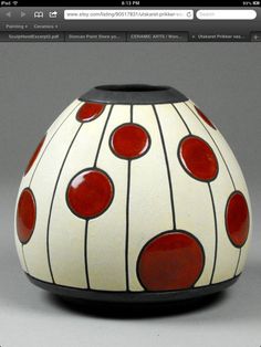 a white vase with red dots on the bottom and black rim, sitting on a gray surface