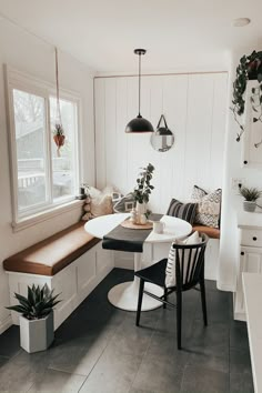 a kitchen table with two chairs and a bench in front of the window, next to a potted plant